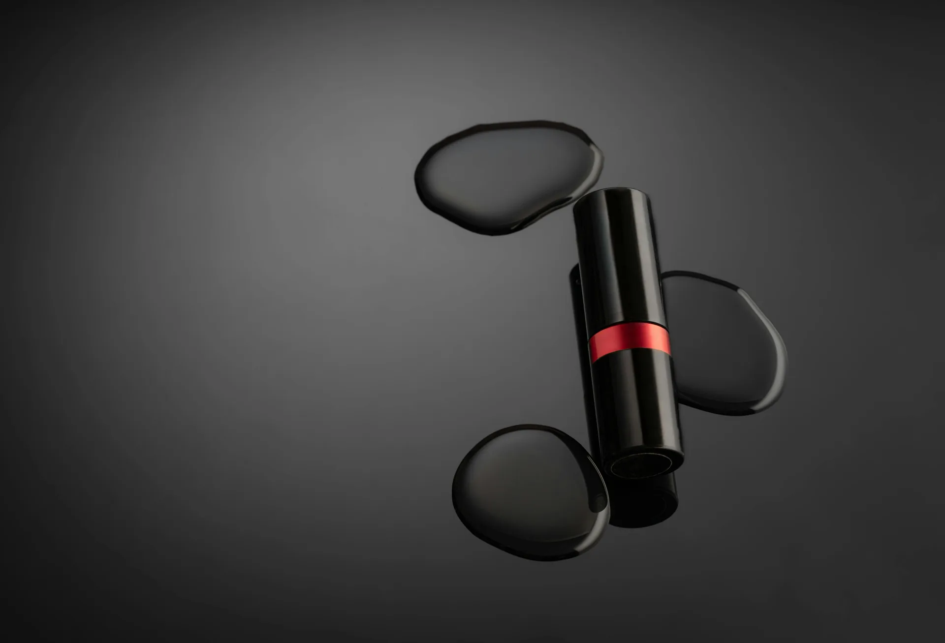 Editorial moody product still-life of a black lipstick with a brand-red ring beside dark water droplets on a glossy surface